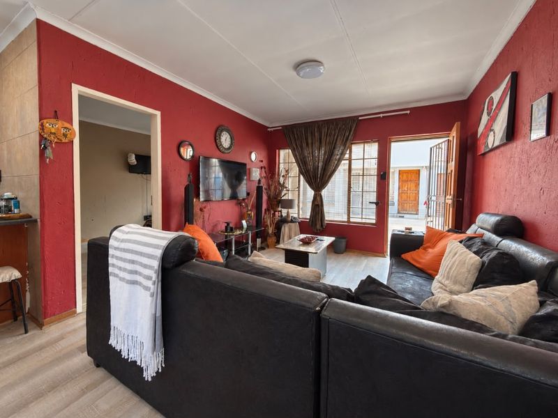A living room featuring textured red walls, laminate flooring, and direct access to an exterior area through a security gate.