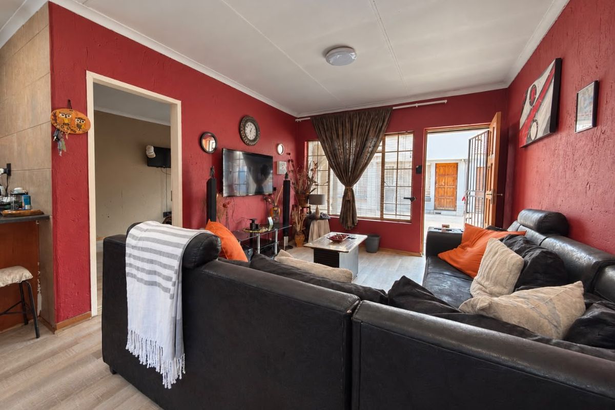 A living room featuring textured red walls, laminate flooring, and direct access to an exterior area through a security gate.