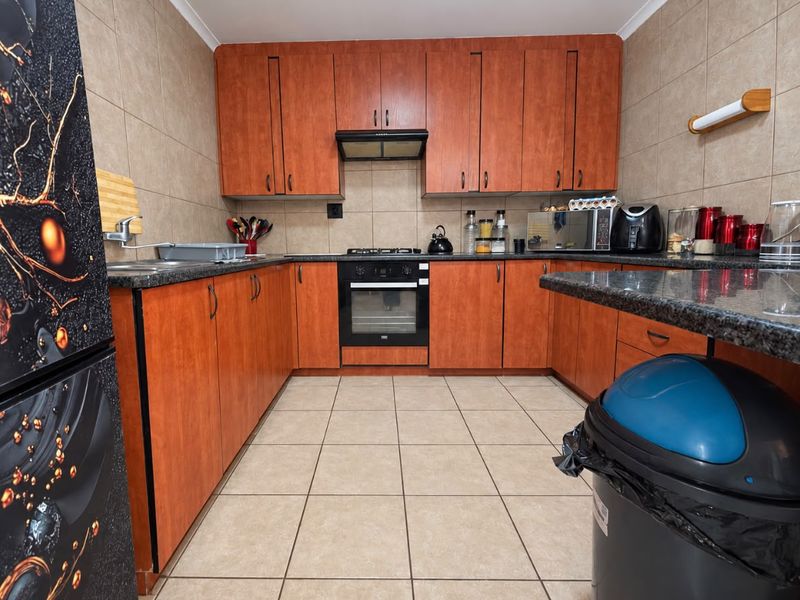 A functional kitchen featuring wood-finish cabinetry, granite countertops, a built-in oven with gas hob, and tiled finishes throughout.