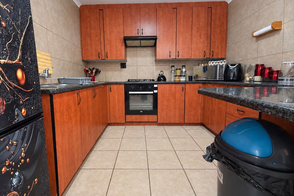 A functional kitchen featuring wood-finish cabinetry, granite countertops, a built-in oven with gas hob, and tiled finishes throughout.
