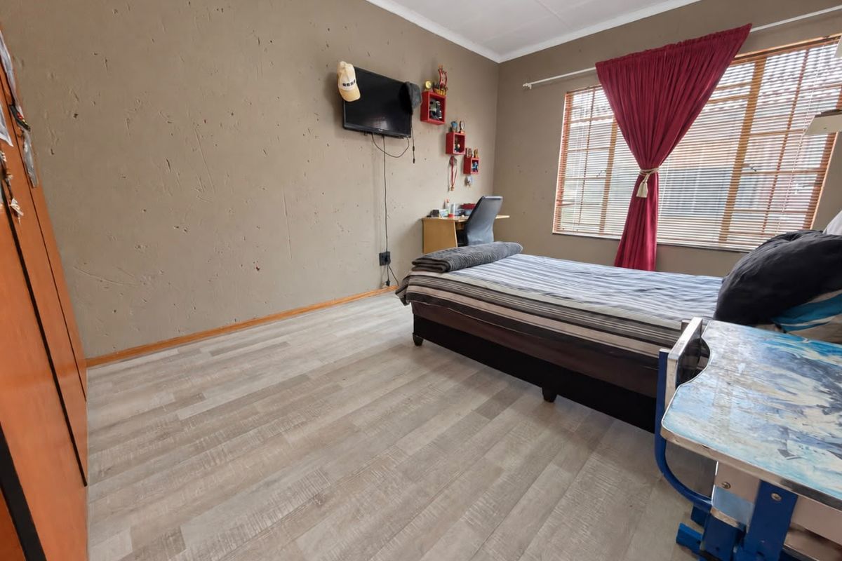 A bedroom featuring light-toned laminate flooring, a built-in wardrobe, and a window with blinds, offering a functional space with potential for cosmetic updates.