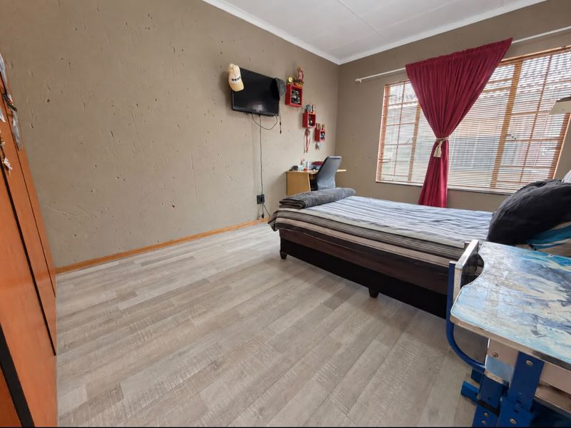 A bedroom featuring light-toned laminate flooring, a built-in wardrobe, and a window with blinds, offering a functional space with potential for cosmetic updates.
