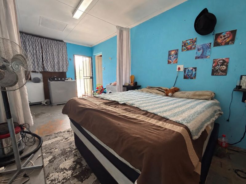 A bedroom space featuring a security gate entrance and basic lighting, currently requiring cosmetic updates to the flooring and wall finishes.