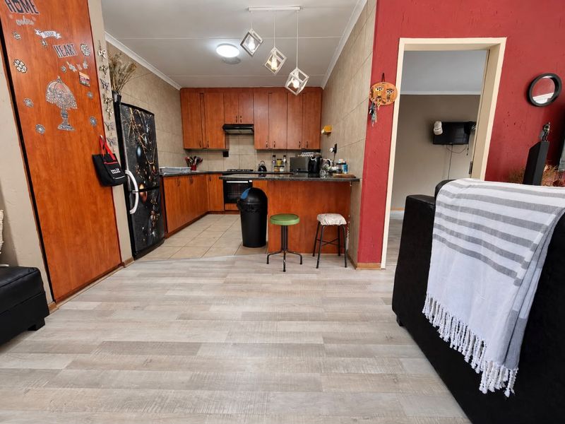 Open plan kitchen and living area featuring wooden cabinetry, granite countertops, built-in oven, and a combination of tiled and laminate flooring.