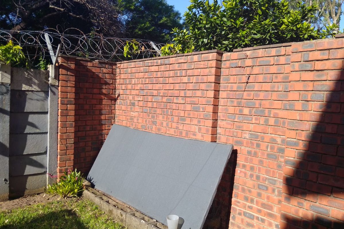 A rear exterior view showing a face brick boundary wall topped with razor wire security fencing and a small grassed area.