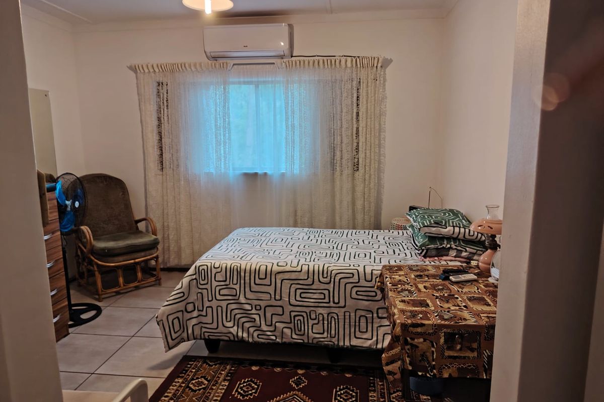 A functional bedroom featuring tiled flooring and a wall-mounted air conditioning unit, providing a comfortable and climate-controlled living space.