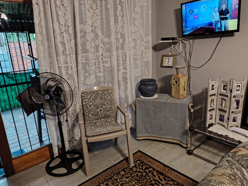 A living area featuring tiled flooring and a sliding glass door leading to an outdoor space, with wall-mounted television and visible electrical cabling.