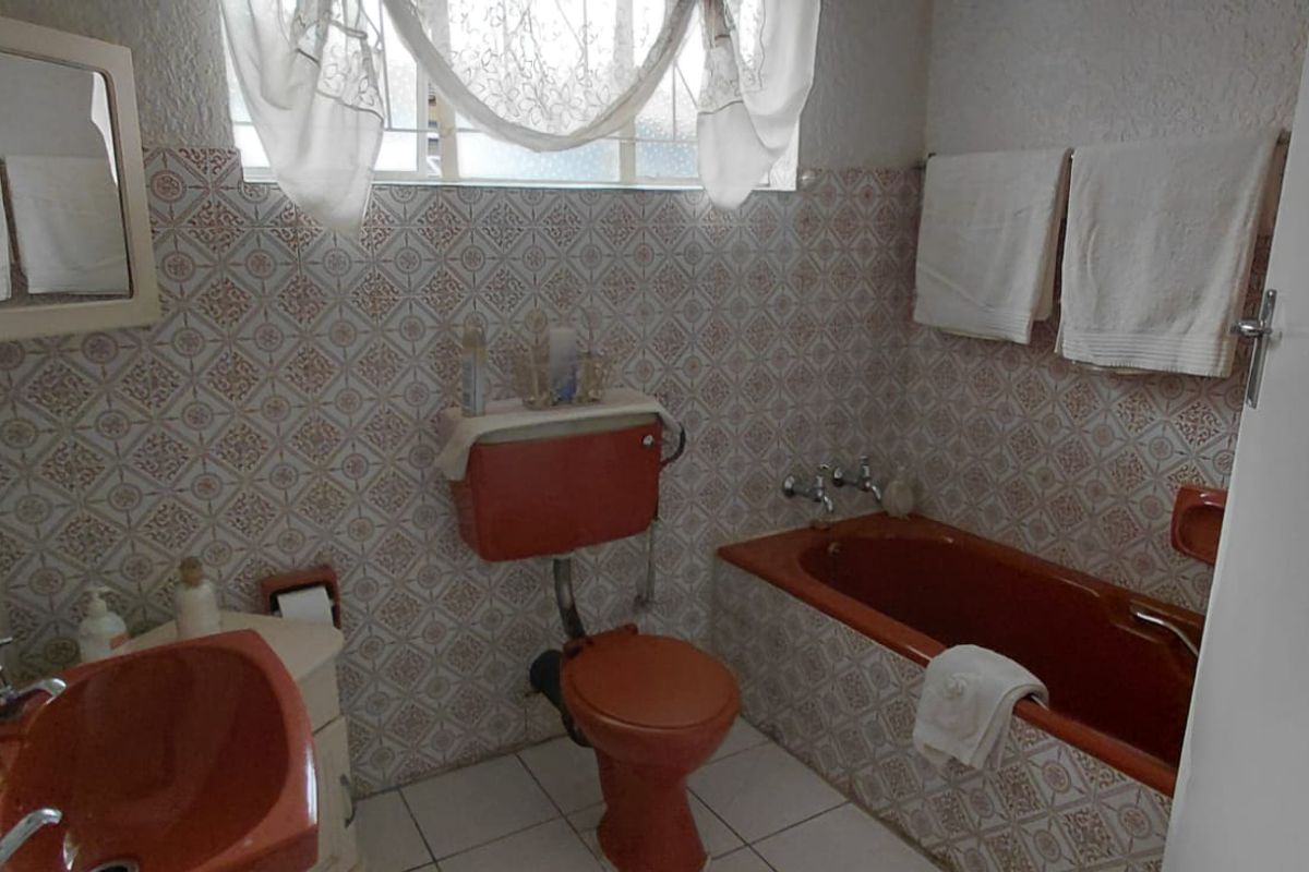 A dated bathroom featuring original colored sanitaryware, patterned wall tiling, and a built-in bathtub, offering significant potential for a modern renovation.