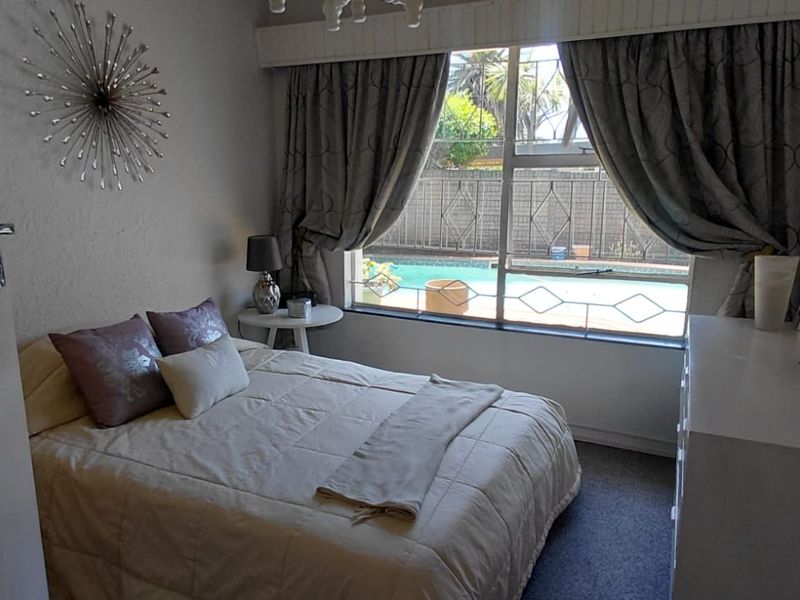 A bedroom featuring carpeted flooring and a window with security bars, offering a view of the outdoor pool area.