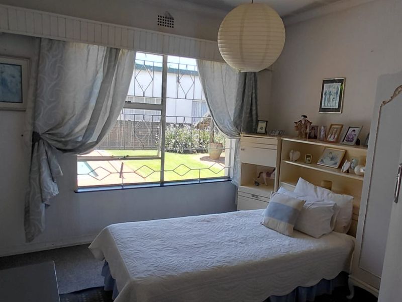 A functional bedroom featuring built-in cupboards and a window with security bars, overlooking the garden area.