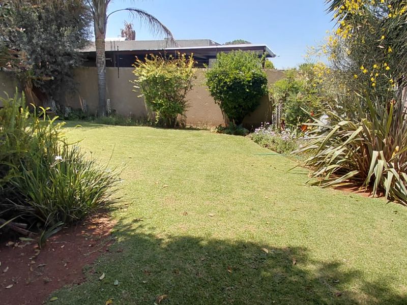 A private rear garden featuring a well-maintained lawn, established shrubs, and secure boundary fencing.