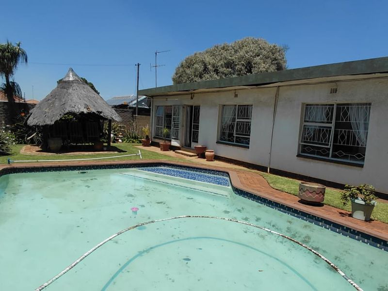 Rear garden area featuring a swimming pool, brick paving, and a traditional thatched lapa structure adjacent to the main house.