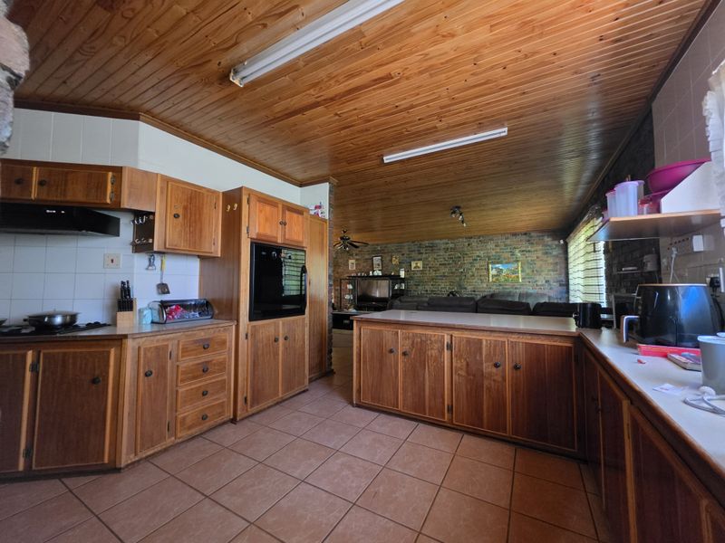 Open plan kitchen and living area featuring timber ceilings, exposed brickwork, tiled floors, and traditional wooden cabinetry with built-in oven and hob.