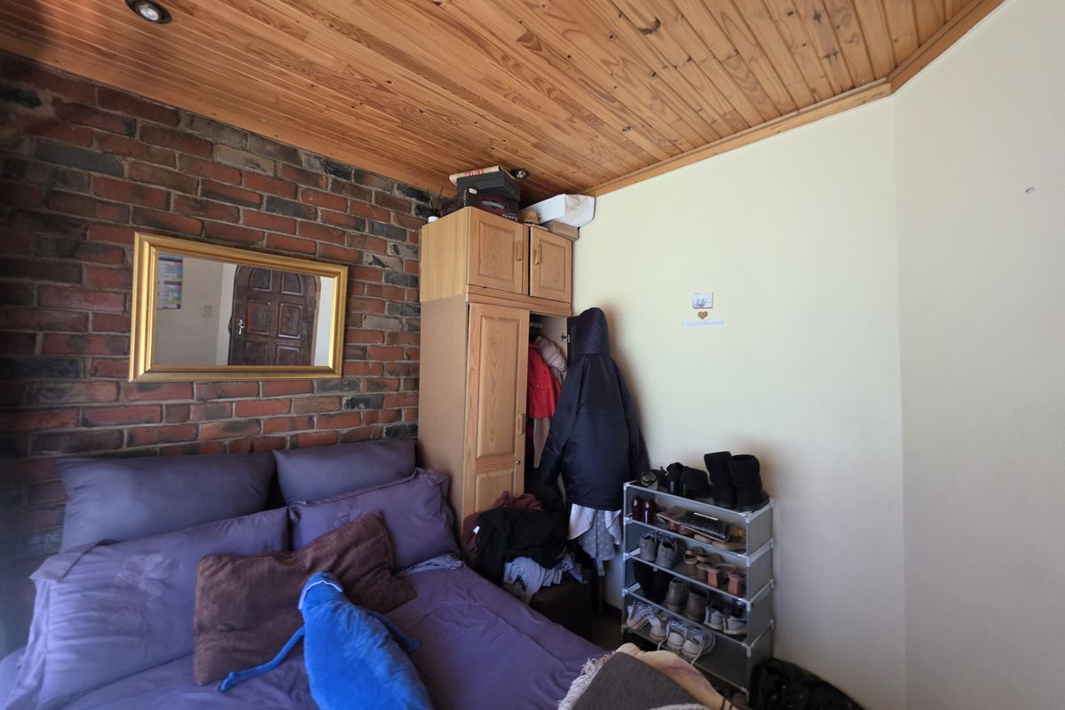 Bedroom featuring an exposed brick feature wall, timber ceiling, and built-in wardrobe storage.