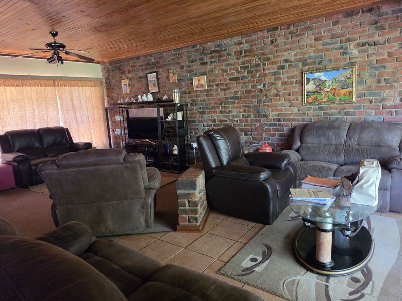 Spacious living room featuring a rustic exposed brick wall, warm timber ceiling, and tiled flooring, offering a cozy and traditional atmosphere.