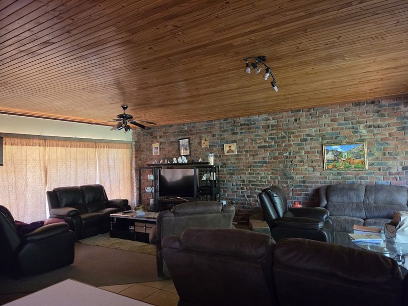 Spacious living room featuring a rustic exposed brick wall and a warm timber tongue and groove ceiling with integrated lighting.