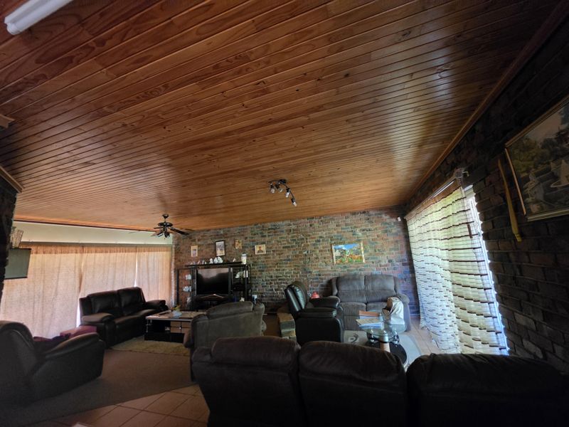 Spacious living room featuring rustic exposed brick walls and a warm timber tongue and groove ceiling with integrated lighting.