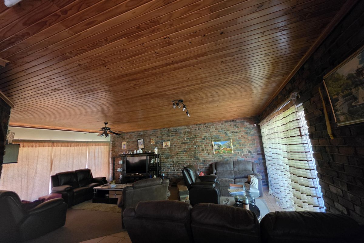 Spacious living room featuring rustic exposed brick walls and a warm timber tongue and groove ceiling with integrated lighting.