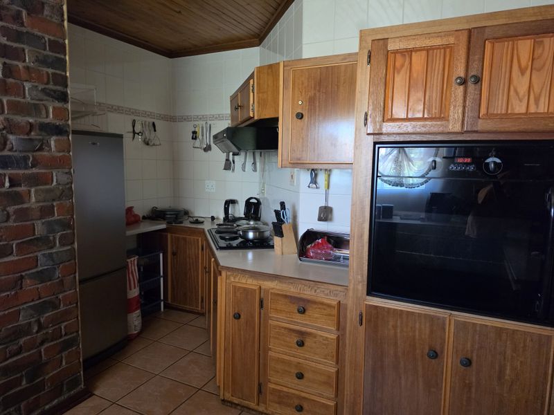 A functional kitchen featuring traditional wooden cabinetry, an exposed brick wall, tiled flooring, and built-in cooking appliances.