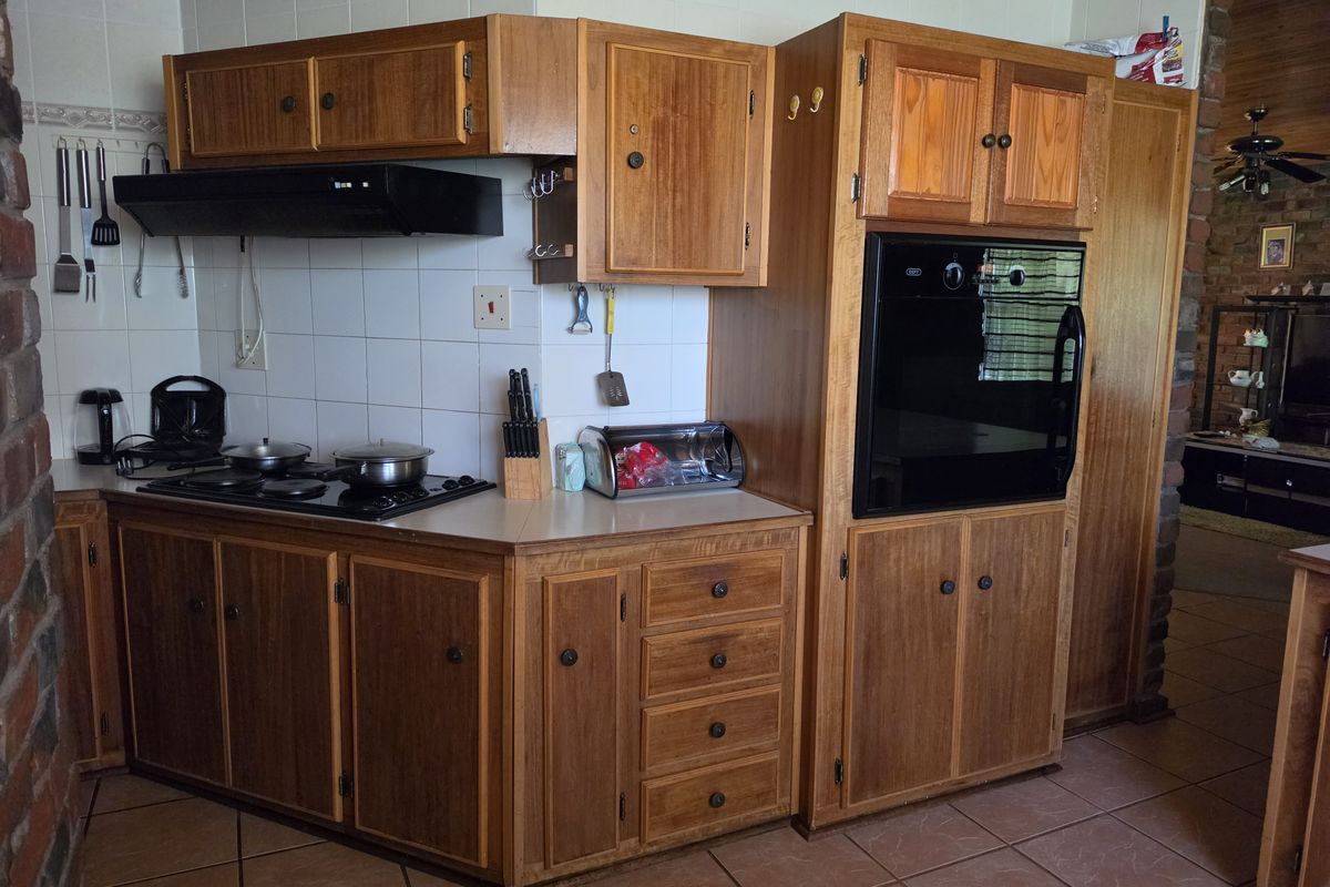 A functional kitchen featuring traditional wooden cabinetry, a built-in oven, a hob with an extractor fan, and tiled finishes throughout.