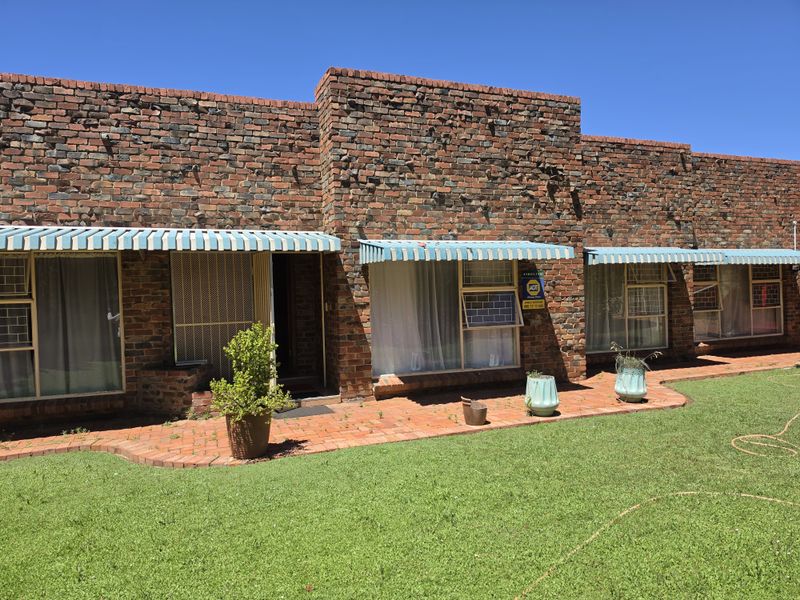 Rear exterior view of a face brick house featuring a paved walkway, lawn area, and striped window awnings.