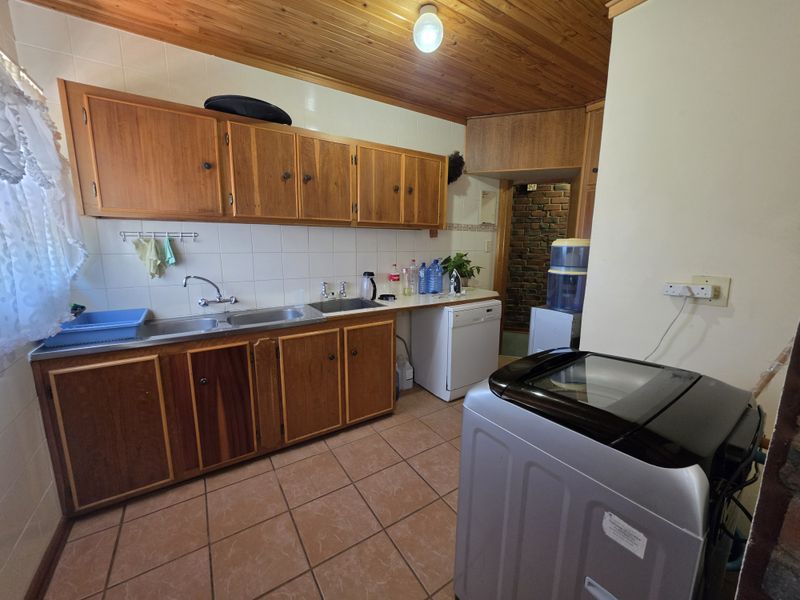 Functional scullery area featuring timber cabinetry, double stainless steel sink, tiled splashback, and timber ceiling, providing practical utility space for the home.