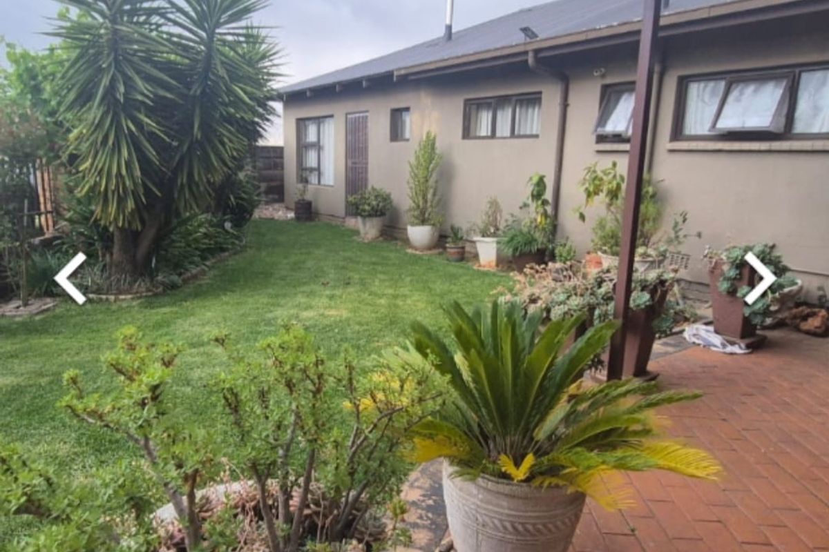 Rear view of the property featuring a brick paved patio, established lawn, and garden area with exterior wall access.