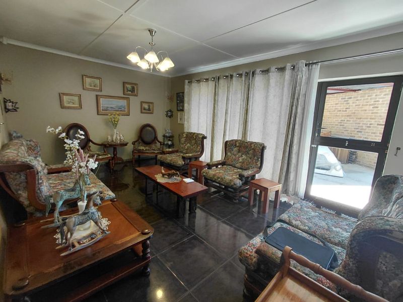 A spacious living room featuring dark tiled flooring and a glass panel door providing access to the exterior.