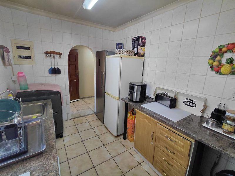 A functional kitchen featuring tiled walls, laminate countertops, and wooden cabinetry, providing a practical workspace with an arched doorway leading to adjacent areas.