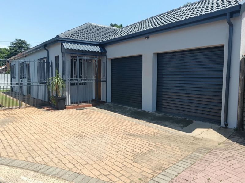 Front exterior view of the property featuring a double garage with roller shutter doors, secure entrance gate, and a paved driveway.