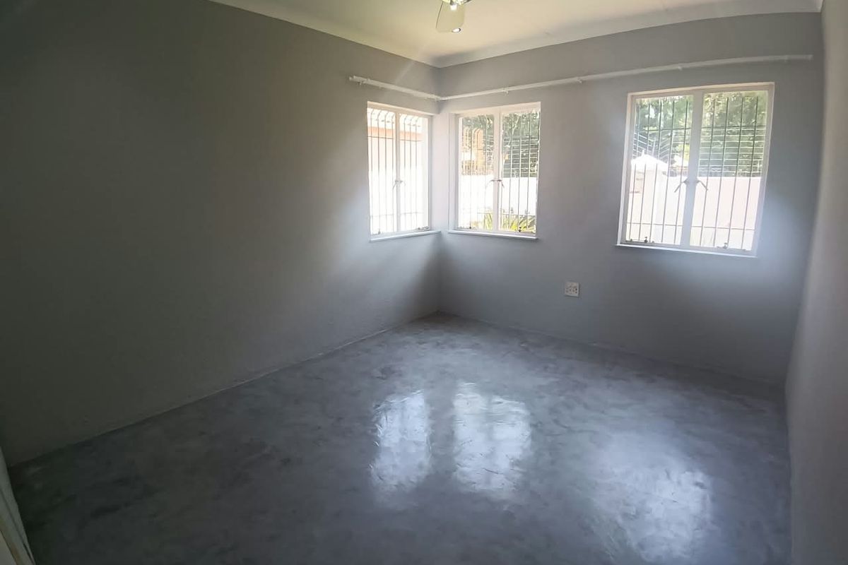 A bright, empty bedroom featuring polished concrete flooring, a ceiling fan, and windows fitted with security bars.