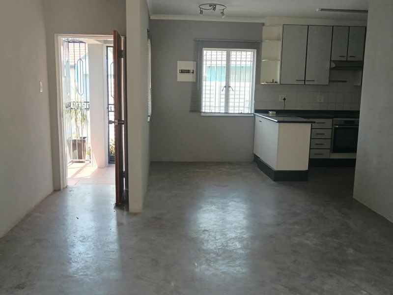 Open plan living area featuring concrete flooring and a functional kitchen with built-in cabinetry, oven, and extractor fan, leading to an outdoor patio area.