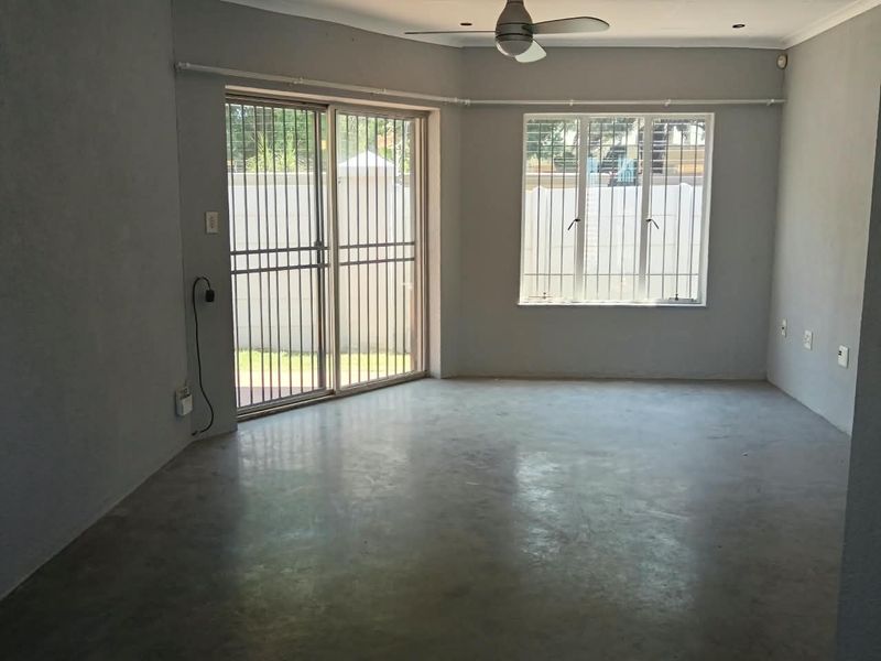 An empty living room featuring concrete flooring, a ceiling fan, and sliding glass doors with security bars, offering a blank canvas for renovation.