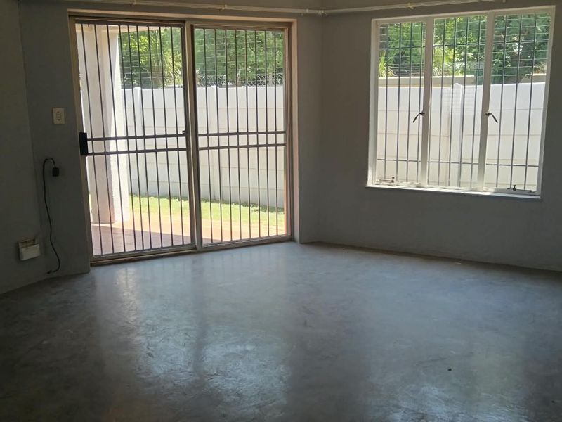 An empty living room featuring polished concrete floors, large windows with security bars, and a sliding glass door leading to the exterior.