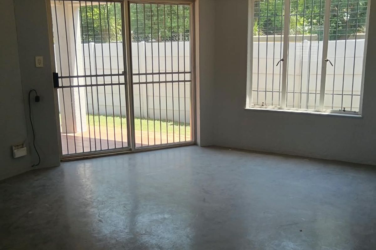 An empty living room featuring polished concrete floors, large windows with security bars, and a sliding glass door leading to the exterior.