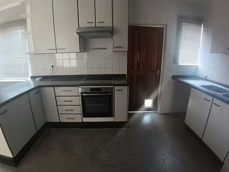 A functional kitchen featuring built-in cabinetry, dark countertops, integrated oven and hob, and a tiled backsplash with direct access to the exterior.