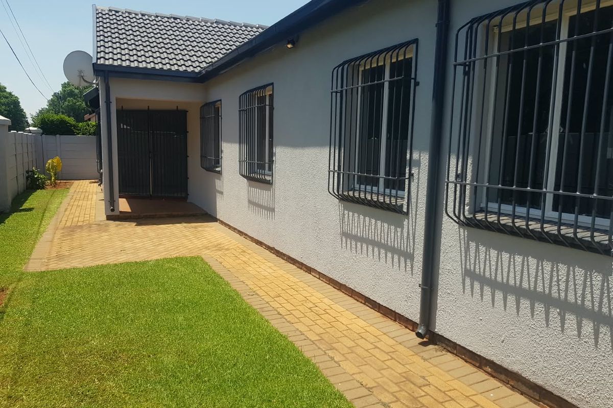 A well-maintained rear exterior view featuring a paved walkway, manicured lawn, and secure windows with fitted security bars.
