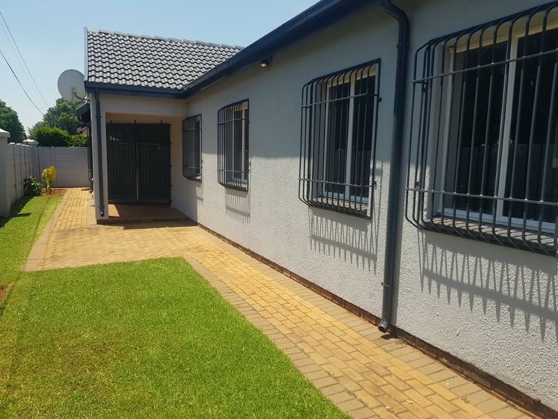 A well-maintained rear exterior view featuring a paved walkway, manicured lawn, and secure windows with fitted security bars.