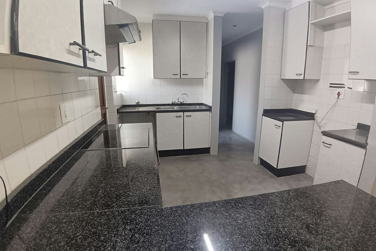 A functional kitchen featuring granite countertops, built-in cabinetry, a stainless steel sink, and an integrated extractor fan with a tiled backsplash.