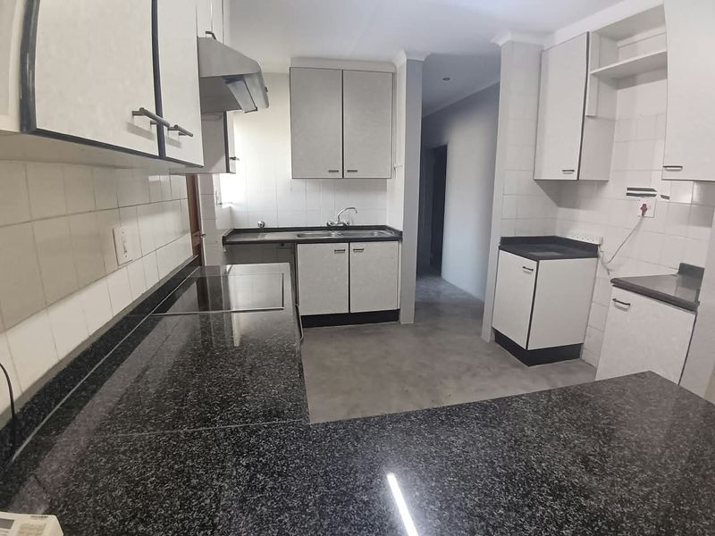 A functional kitchen featuring granite countertops, built-in cabinetry, a stainless steel sink, and an integrated extractor fan with a tiled backsplash.