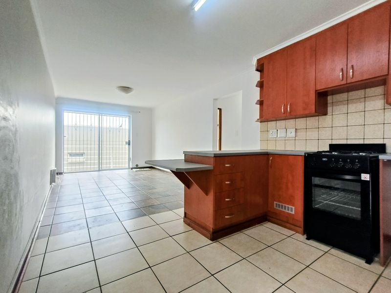 An open-plan kitchen and living area featuring tiled flooring, built-in wooden cabinetry, and a sliding glass door leading to the exterior.