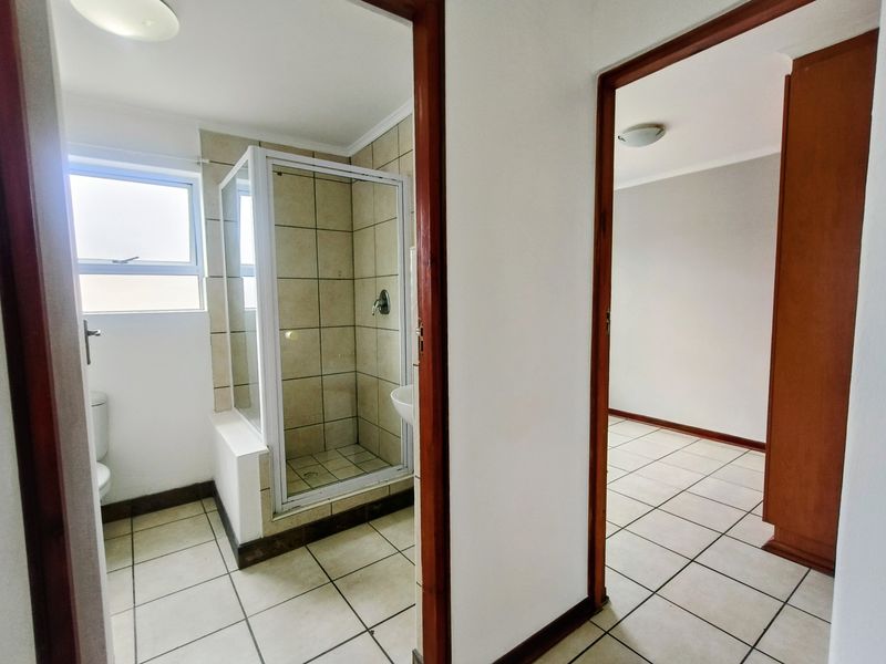 A functional bathroom featuring a shower enclosure and tiled flooring, adjacent to an empty room with matching floor tiles.