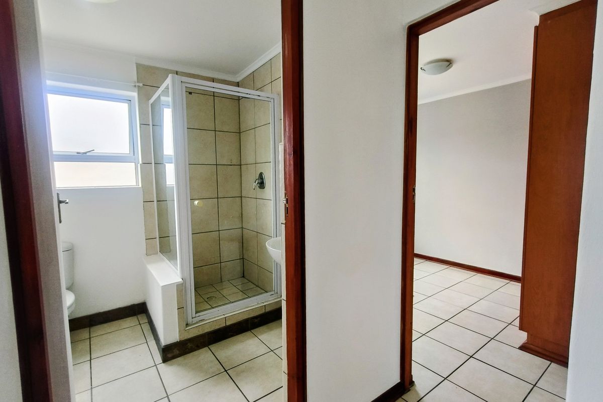 A functional bathroom featuring a shower enclosure and tiled flooring, adjacent to an empty room with matching floor tiles.