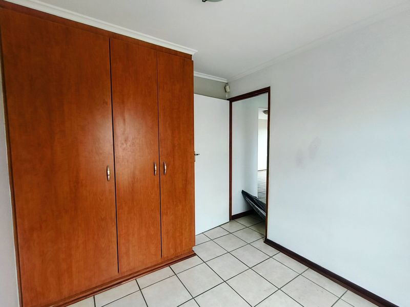 A clean, empty bedroom featuring built-in wooden cupboards and neutral tiled flooring, offering a blank canvas for personalization.