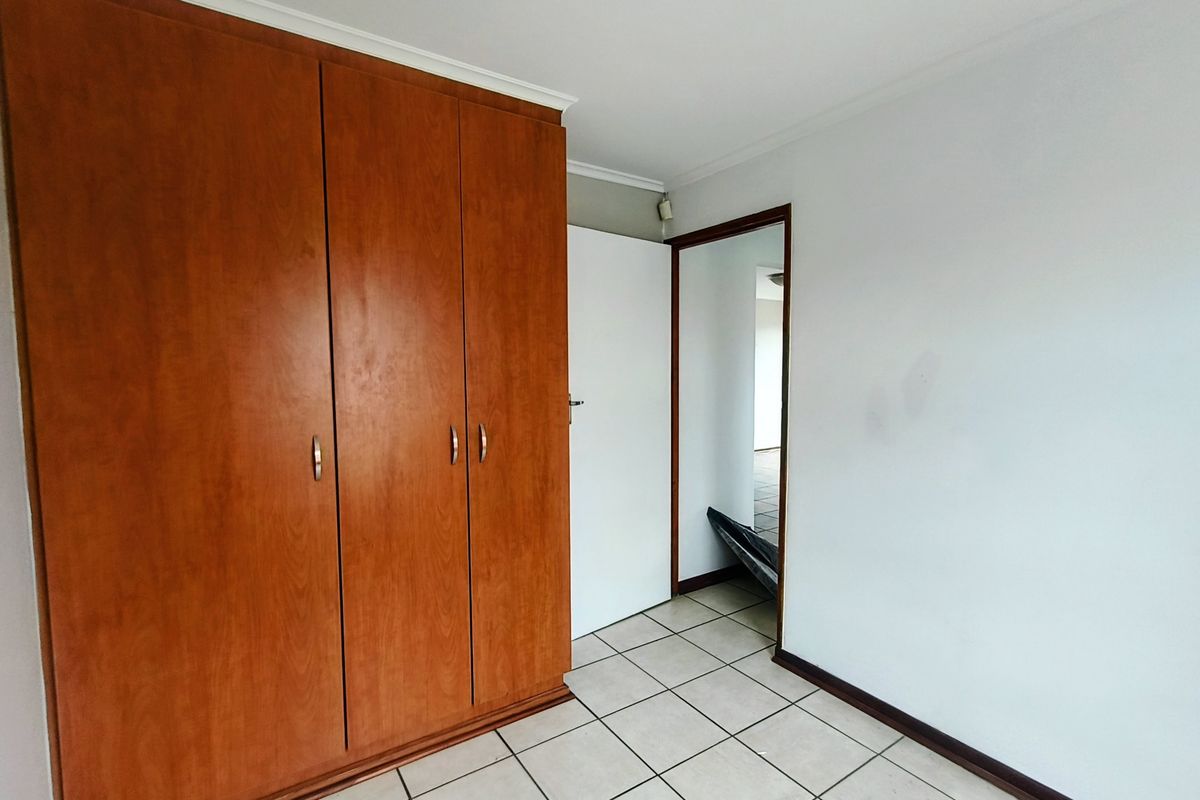 A clean, empty bedroom featuring built-in wooden cupboards and neutral tiled flooring, offering a blank canvas for personalization.