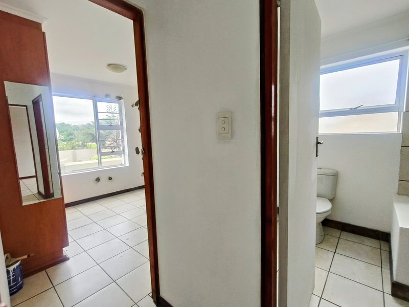 A view from a hallway looking into an empty bedroom and a bathroom, featuring tiled floors and aluminium window frames.