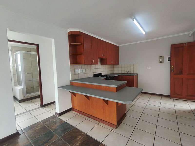 Open plan kitchen featuring wooden cabinetry, a breakfast bar, and tiled flooring, with an adjacent view into a tiled bathroom area.