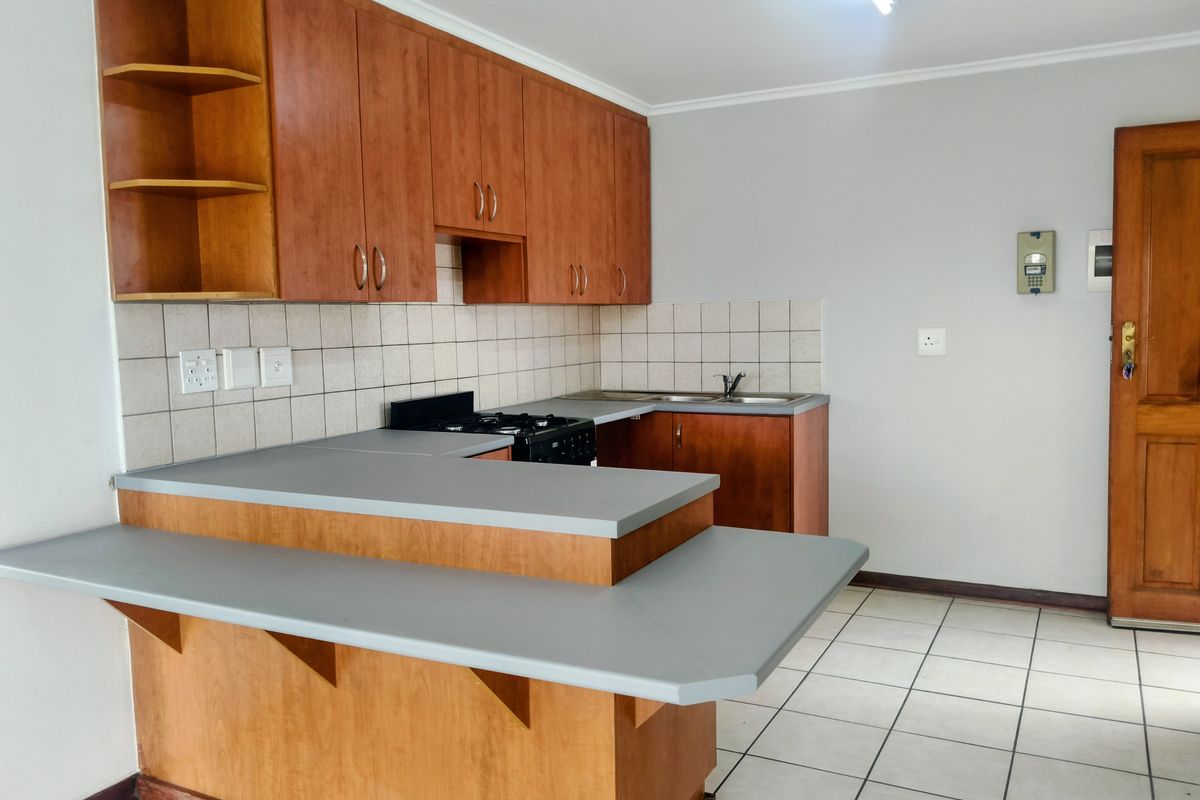 A functional kitchen featuring wooden cabinetry, laminate countertops, a built-in stove, and tiled flooring, offering a clean and practical workspace.