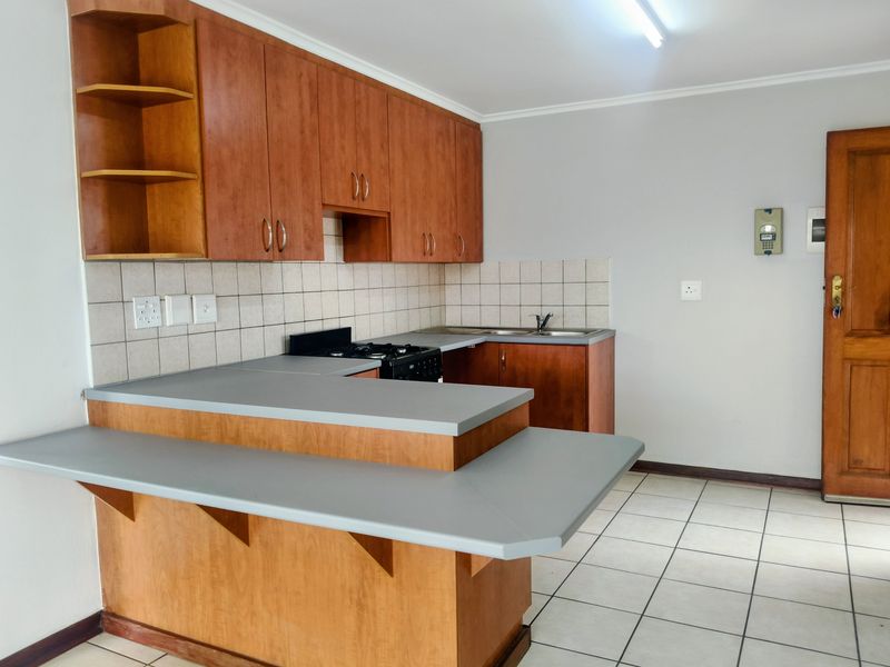 A functional kitchen featuring wooden cabinetry, laminate countertops, a built-in stove, and tiled flooring, offering a clean and practical workspace.