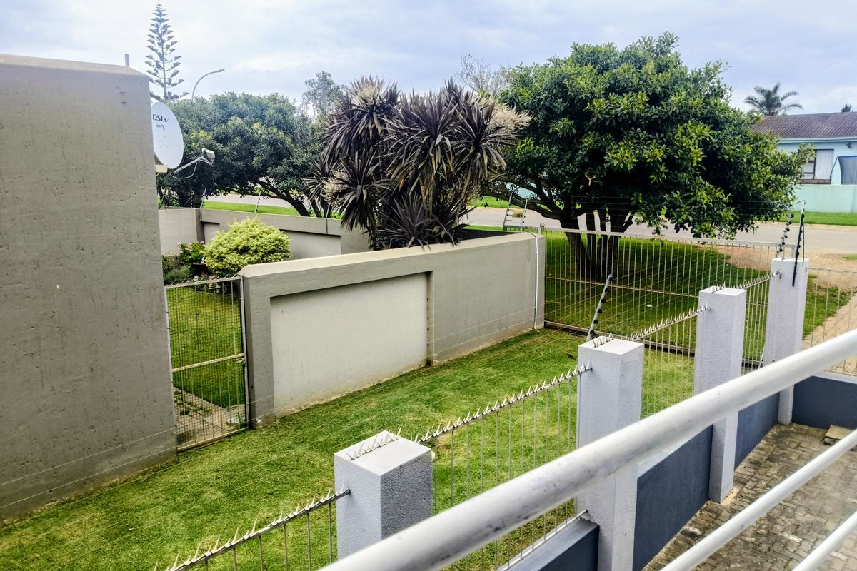 A view of the rear garden area featuring a lawn, boundary walls with electric fencing, and a paved section.